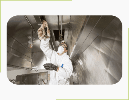 A man in white suit and black gloves working in a restaurant cleaning the kitchen hoods.